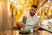 Bearded professional chef in white uniform with dispenser adding cream on portion of gourmet sea urchin in fine dish restaurant