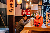 Junge asiatische Frau im Pullover isst Ramen mit Löffel an einem Holztresen in einem Cafe
