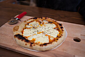 Frische hausgemachte dampfend heiße gebackene Pizza mit geschmolzenem Mozzarella-Käse und Sauce und knusprigem Rand auf Schneidebrett in heller Küche serviert