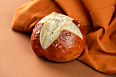 From above fresh salty pretzel bun placed near orange cloth on brown background
