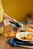 Crop anonymous woman putting delicious healthy homemade dish with pumpkin and tomatoes on plate standing at table in kitchen