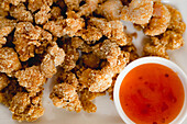 Closeup pieces of crispy roasted chicken placed near bowl with yummy sauce on white background