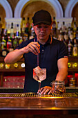 Young Asian bartender stirring a gin tonic cocktail with a spoon in the bar