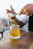 Crop anonymous bartender sifting powder to whiskey smash cocktail with ice cubes at counter