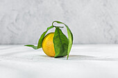 Orange citrus tangerine with verdant stem and leaf lying on white table