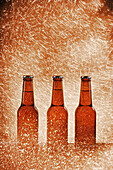 Glass bottle of cold beer surrounded by sparkling lights on bright background