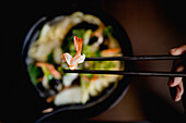 Top view of bowl of tasty oriental noodle soup with fresh prawns placed on table against black background