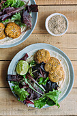 Plates with fresh lettuce salad and sweet potato falafel near sauce and sesame on wooden table