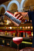 Detail of unrecognizable bartender's hand working in the bar with his shaker and pouring a cocktail in the glass