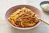 A plate of authentic Italian spaghetti carbonara, garnished with grated cheese and pieces of crispy bacon.