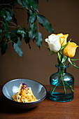 Cheese and walnuts tortellini in a black bowl, garnished with microgreens, beside a vase with yellow roses.