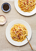 Ansicht von oben auf traditionelle italienische Spaghetti Carbonara mit geriebenem Käse auf einem sauberen, strukturierten Tischtuch.