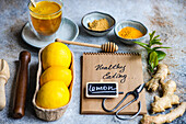 Ein Wellness-Setup mit Zitronen, Ingwer, Honig und Gewürzen sowie einem Notizblock mit der Aufschrift "Gesunde Ernährung", der zur Planung einer gesunden Mahlzeit inspirieren soll