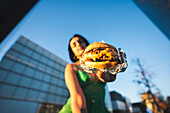 A woman in urban Madrid showcases a juicy burger against the backdrop of the Four Towers business area.