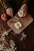A close-up view of aged hands cutting a fresh apple on a rustic wooden cutting board, with a serene and homely atmosphere