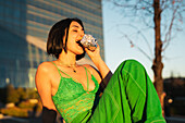 A stylish young woman bites into a foil-wrapped snack, contrasting with the modern backdrop of the Cuatro Torres business area in Madrid.