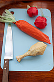 Colorful plastic bags are twisted to resemble food items, placed on a blue cutting board beside a knife.