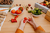 Hands sorting cherry tomatoes with assorted fresh vegetables on a wooden table, prepping for a healthy meal
