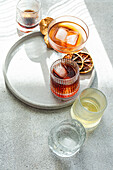 Draufsicht auf verschiedene alkoholische Getränke in strukturierten Gläsern auf einem runden Betontablett, mit Schattenwurf durch das helle Tageslicht