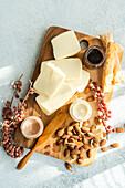 A gourmet cheese platter featuring various cheeses, almonds, honeycomb, and preserves on a rustic wooden board with a textured light backdrop