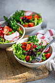 A trio of appetizing vegetable salads with lettuce, arugula, radishes, cherry tomatoes, green onions, and pomegranate seeds on a wooden board