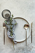 An elegant table setting featuring a white plate, silverware, and natural greenery for a sophisticated dining experience