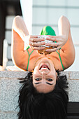 An exuberant young woman smiles while lying upside down with Madrid's iconic Four Towers in the backdrop, reflecting a vibrant urban life.