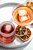 Vibrant alcoholic drinks served in textured glasses, accented with ice cubes and garnished with dehydrated orange slices on a sunny day