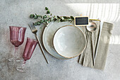Stylish table setting with vintage-inspired glassware, cutlery, and plates, accented by natural greenery