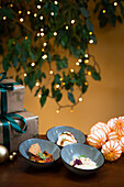 Drei elegante Canapés werden auf kleinen Tellern vor einem warmen, festlichen Hintergrund mit funkelnden Lichtern und Geschenkboxen präsentiert.