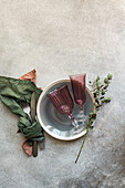 Ein raffiniert gedeckter Tisch mit zwei burgunderroten Weingläsern in einer silbernen Schale, begleitet von frischem Grün auf einer strukturierten Oberfläche