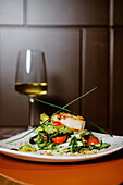 Elegante Präsentation eines Gourmetsalats mit Kirschtomaten, serviert auf einem stilvollen Teller mit einem Glas Weißwein im Hintergrund