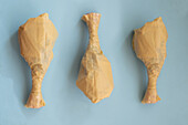 From above three pieces of chicken food sculpted from plastic bags, resembling meat cuts, presented on a plain blue background.