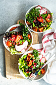 Top view of fresh vegetable salads with lettuce, arugula, radishes, cherry tomatoes, and pomegranate seeds on a wooden board with a kitchen towel