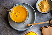 Ein warmer, goldener Kurkuma-Latte in einer Keramiktasse, begleitet von einer Schale mit Kurkumapulver und einem Honiglöffel, vermittelt eine gemütliche, gesunde Atmosphäre