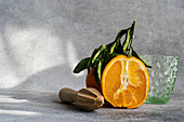 Ein verlockendes Bild, das eine halbierte Orange mit einer hölzernen Saftpresse und einem leeren Glas zeigt, alles vor einem strukturierten grauen Hintergrund, der eine natürliche und frische Atmosphäre hervorruft