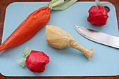 Colorful plastic bags are twisted to resemble food items, placed on a blue cutting board beside a knife.