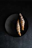 Artistic top view of two sugar-dusted, homemade jam-filled pastries on a dark round plate against a black textured background