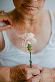 A poignant close-up of an elderly woman's hands holding a white flower, symbolizing fragility and the passage of time