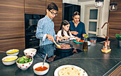 A mother and her children prepare a taco dinner in the kitchen, with the son cooking meat and the daughter chopping tomatoes
