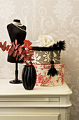 Bust, boxes and black vase with decorative branches on a white chest of drawers in front of wallpaper