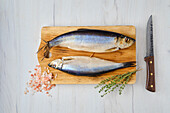 Raw herrings on wooden board with herbs