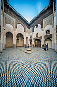 Visitors in the ornate courtyard of Madrasa Cherratine under a clear blue sky.