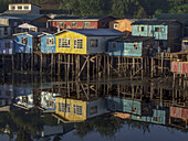 Bunte Palafitos oder Stelzenhäuser der Fischer spiegeln sich bei Sonnenaufgang in einer Bucht in Castro auf der Insel Chiloe, Chile.