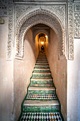 A person ascends the ornate staircase adorned with mosaic tiles in Fez's historical Cherratine Madrasa.