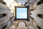 A serene look up into the sky framed by the ornate architecture of Cherratine Madrasa, Fez, Morocco