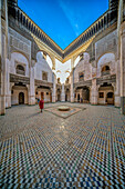A person strolls through the ornate courtyard of Madrasa Cherratine under a clear blue sky.