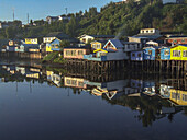 Bunte Palafitos oder Stelzenhäuser der Fischer spiegeln sich bei Sonnenaufgang in einer Bucht in Castro auf der Insel Chiloe, Chile.