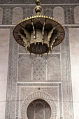 A bronze lamp hangs against the intricate tiled backdrop of Cherratine Madrasa., Fez, Morocco.