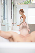 Mann entspannt sich in der Badewanne, Frau im Hintergrund